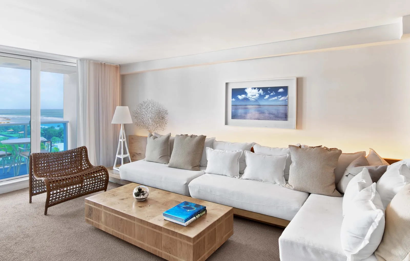 A suite's living room, a white sectional beneath framed coastal art, sliding glass open to the balcony.