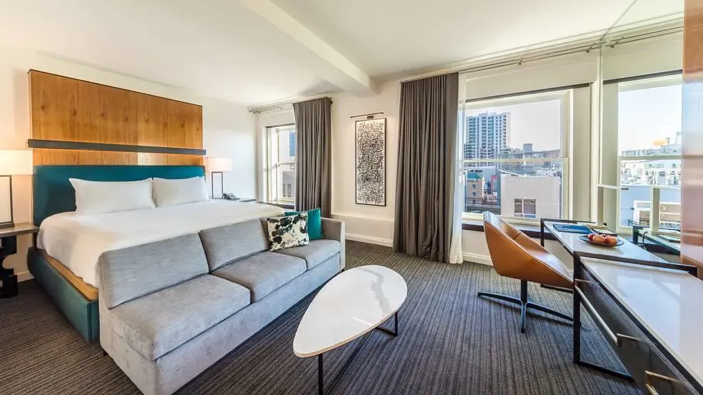 A room with a teal headboard and corner windows over downtown rooftops.