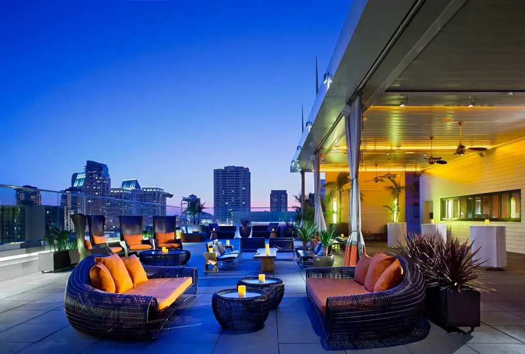 The rooftop at dusk, wicker daybeds and candles against the downtown skyline.