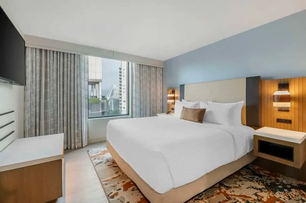 A king room in pale blue, slatted wood bedside panel, window onto downtown.