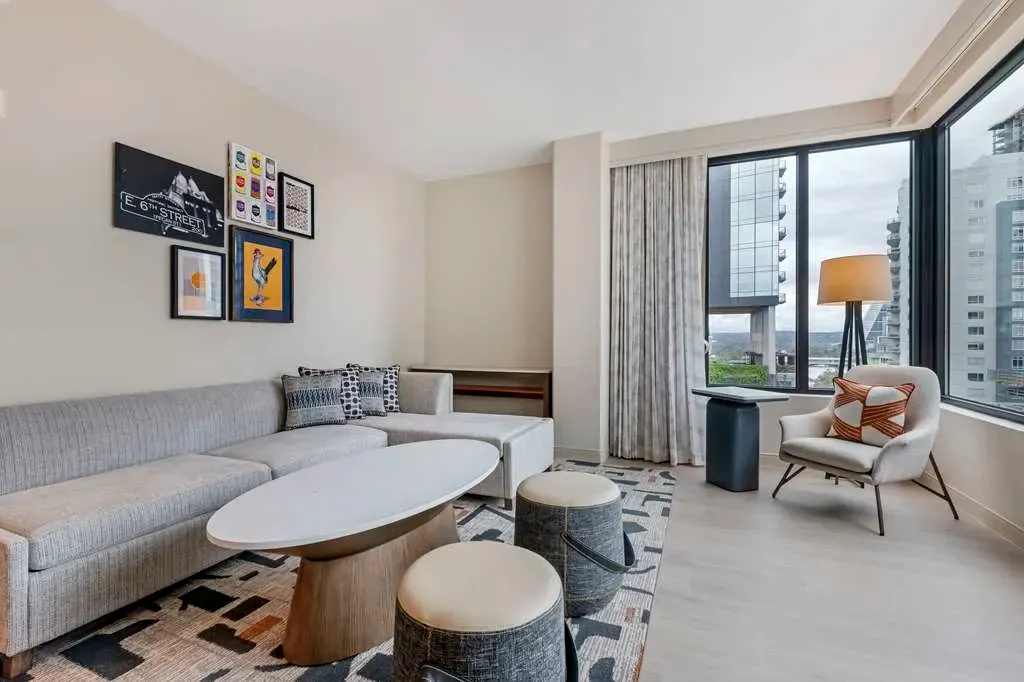 A suite living room, a long sofa under framed Austin prints, corner windows.