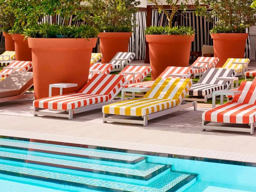 Red, yellow, and black-striped loungers between oversized terracotta planters at the pool's edge.