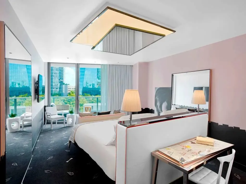 A guest room in Philippe Starck's design, pink walls and a black handprint-patterned carpet beneath an angled mirrored ceiling fixture.