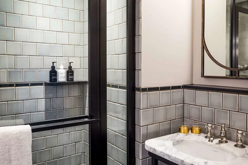 Sage and gray tile, a black-framed walk-in shower and an arched mirror.