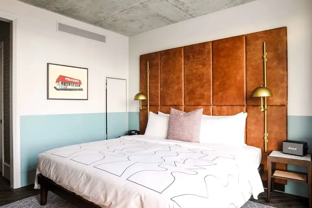 A room under bare concrete, tan leather headboard and brass swing-arm lamps.