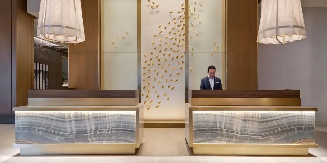 Backlit onyx reception counters, gilded birds climbing the panel between them.
