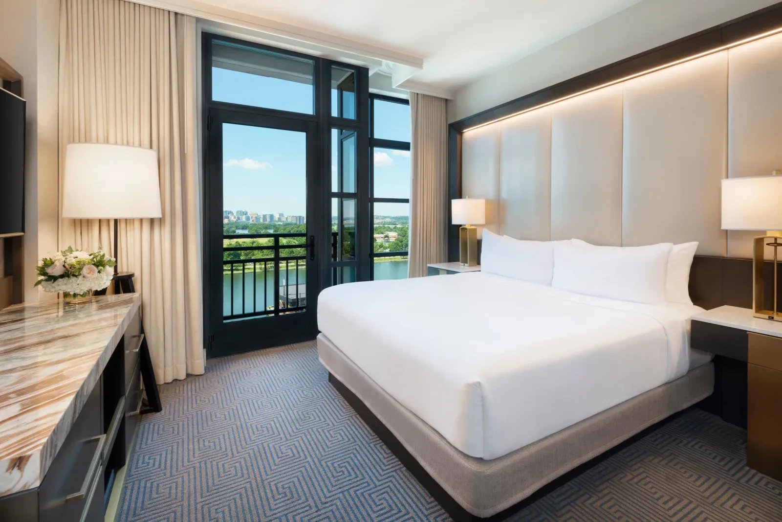 A king room with a lit cream headboard, balcony doors onto the water.