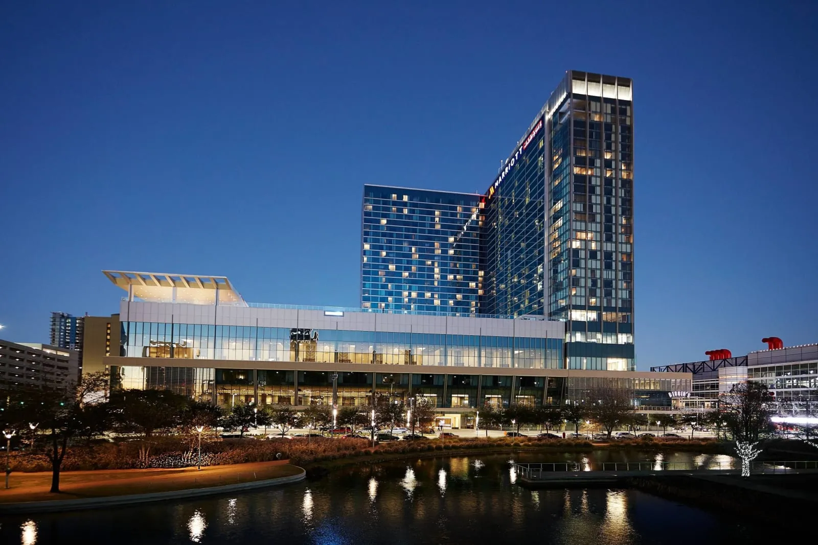 The tower at blue hour above Discovery Green, lit windows on the water.