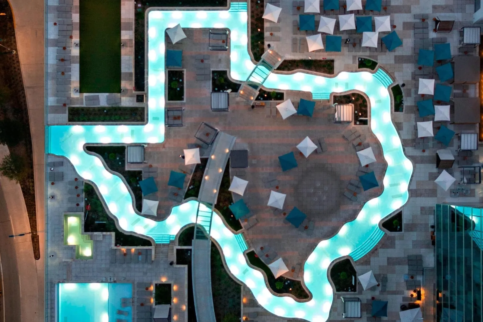 The Texas-shaped lazy river lit turquoise at dusk, seen from straight above.