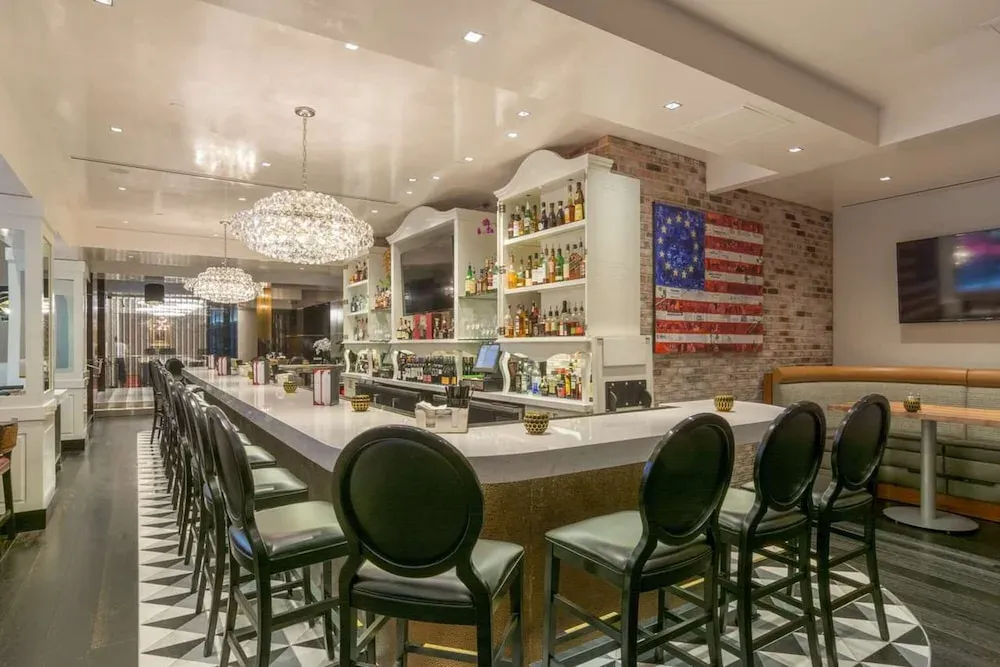 The indoor bar, black leather stools on checkered tile under crystal chandeliers.