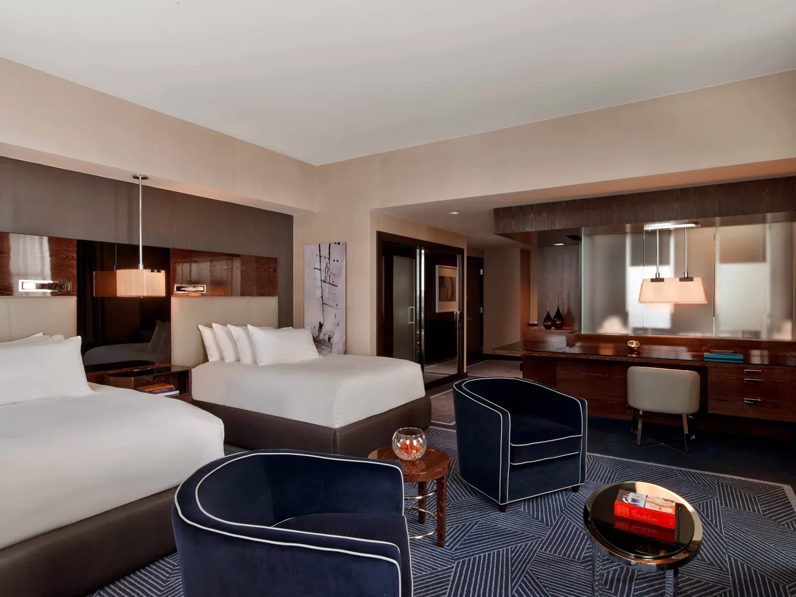 Two beds against a lacquered wood wall, navy chairs on a chevron rug.