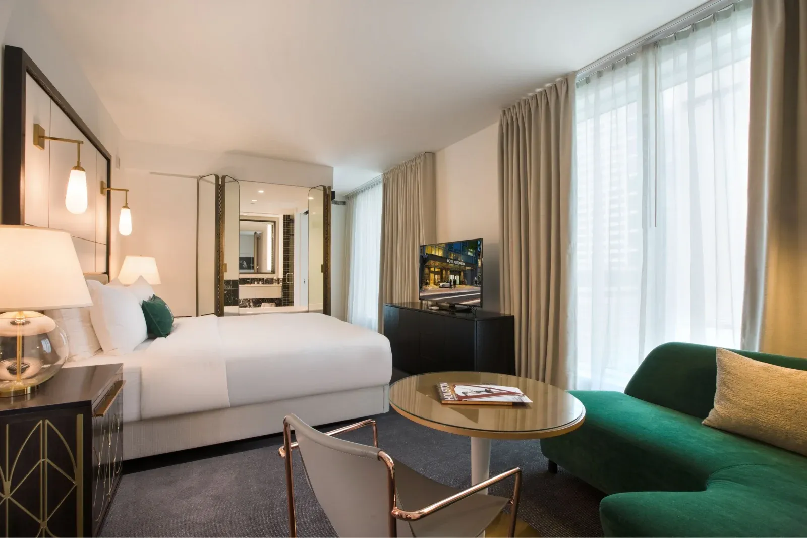 A deluxe room in cream and brass, green velvet chaise by the window.