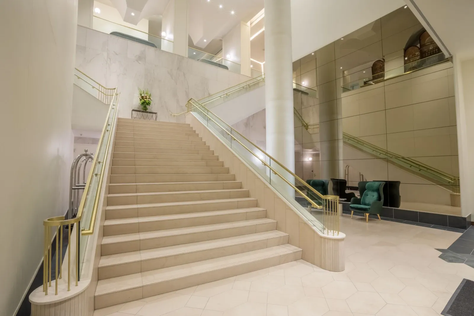 The lobby's marble staircase under brass and glass rails, mirrored wall alongside.