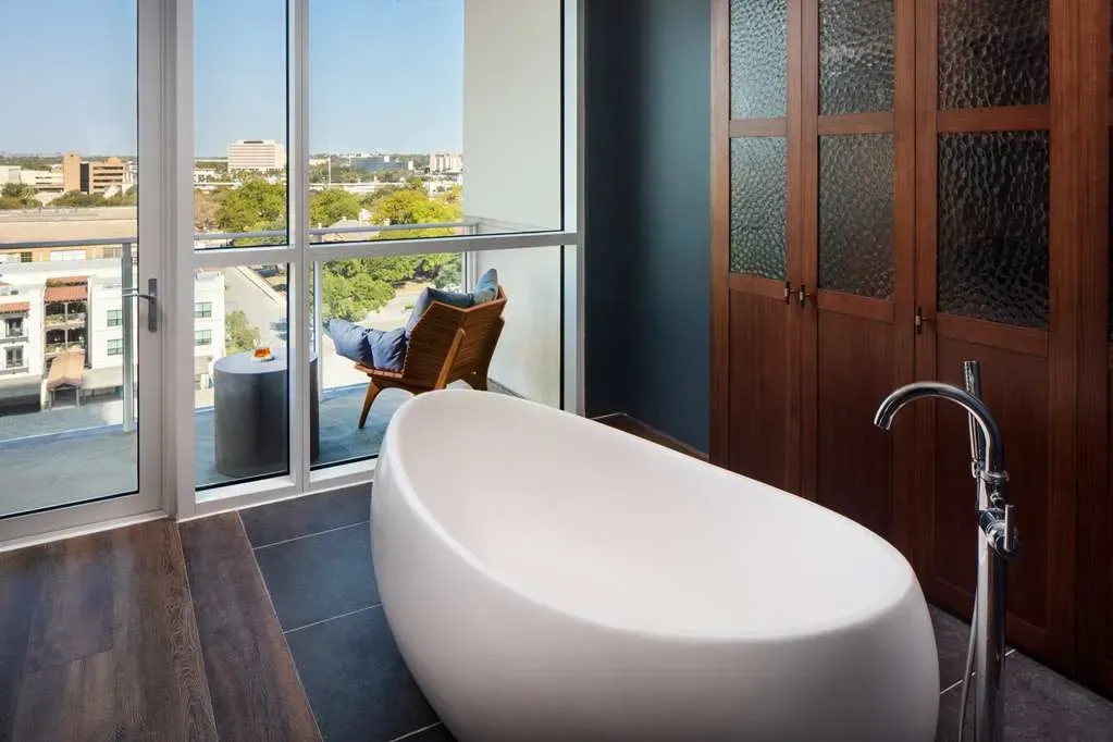 A freestanding oval tub beside floor-to-ceiling glass and the balcony.