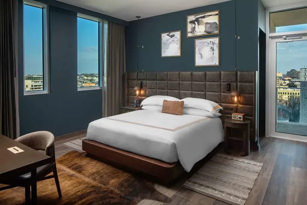 A king room in deep teal, leather grid headboard, windows onto the city.