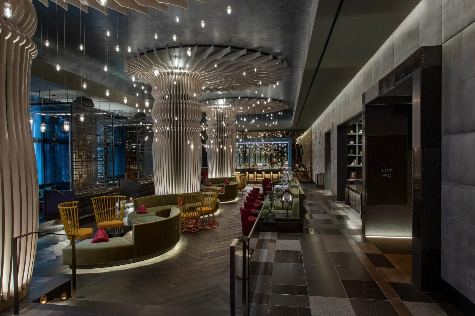 The lobby, fluted white columns beneath a canopy of hanging bulbs, olive banquettes.