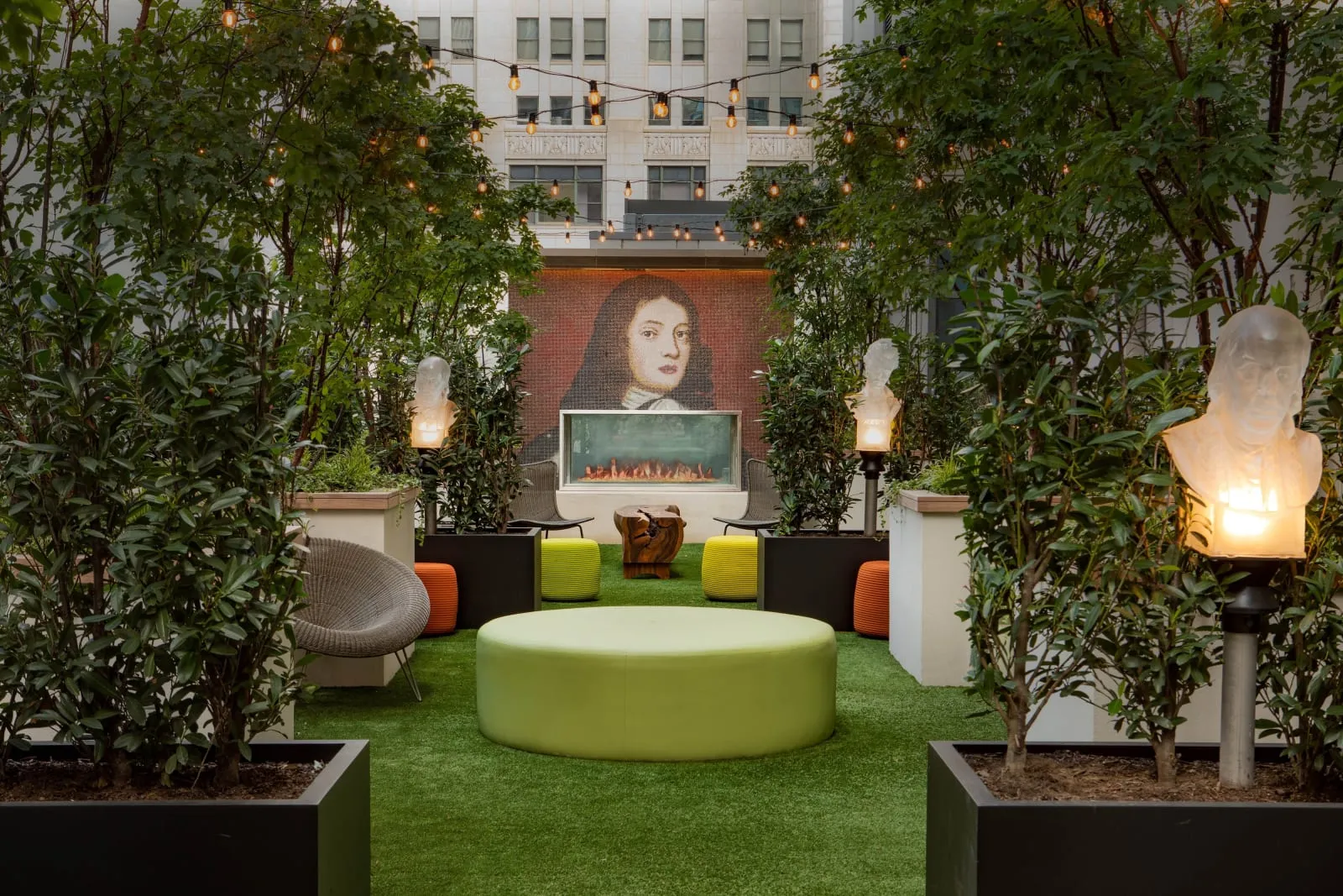 The garden terrace, string lights over turf, a fireplace and lit busts among the planters.